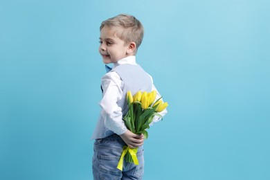 Cute little boy with bouquet of tulips on light blue background