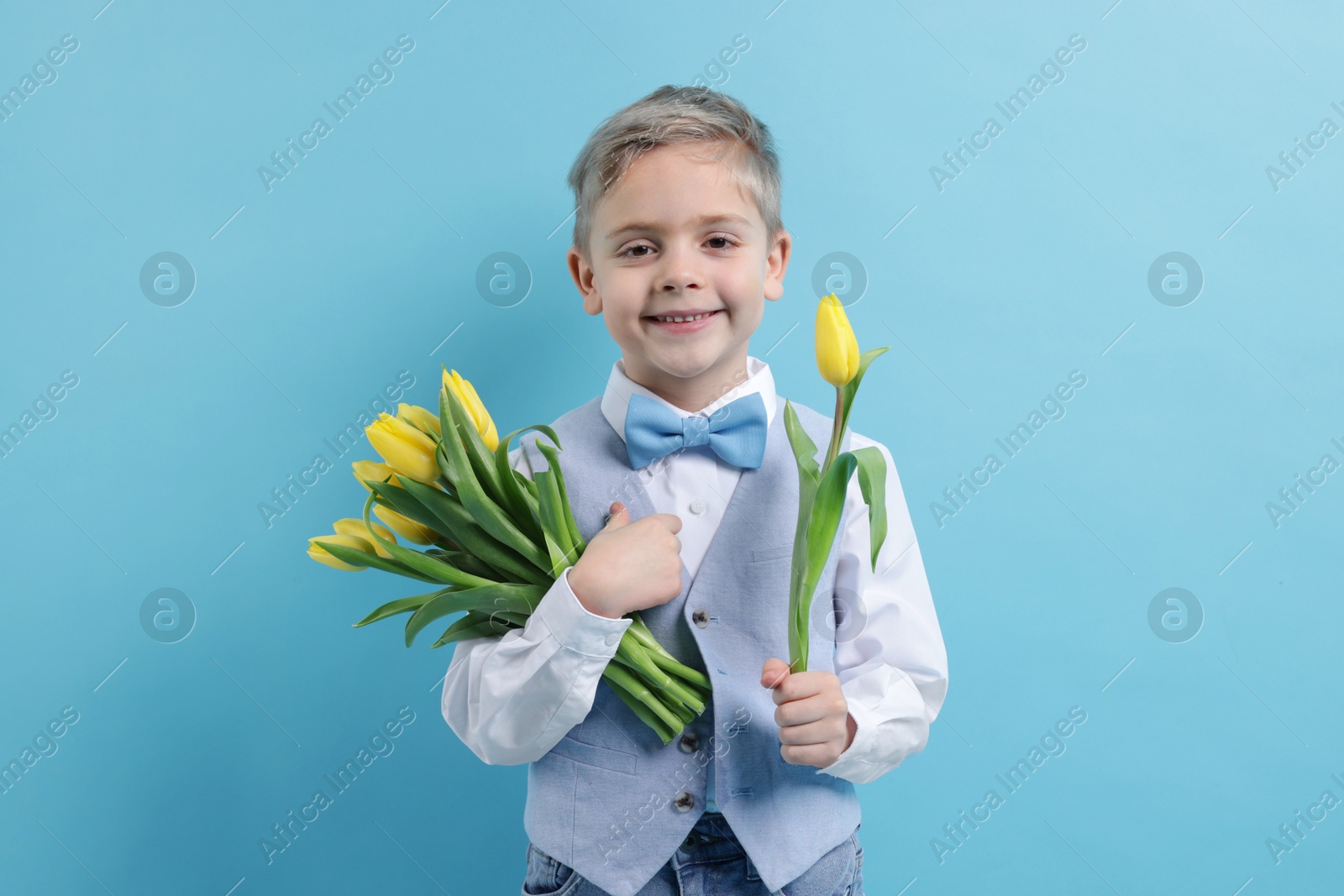 Photo of Cute little boy with bouquet of tulips on light blue background