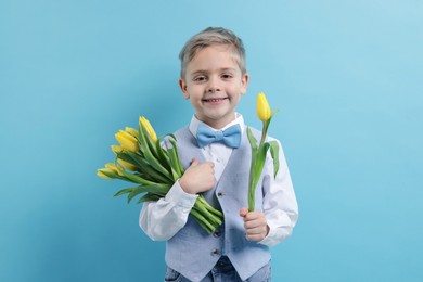 Cute little boy with bouquet of tulips on light blue background