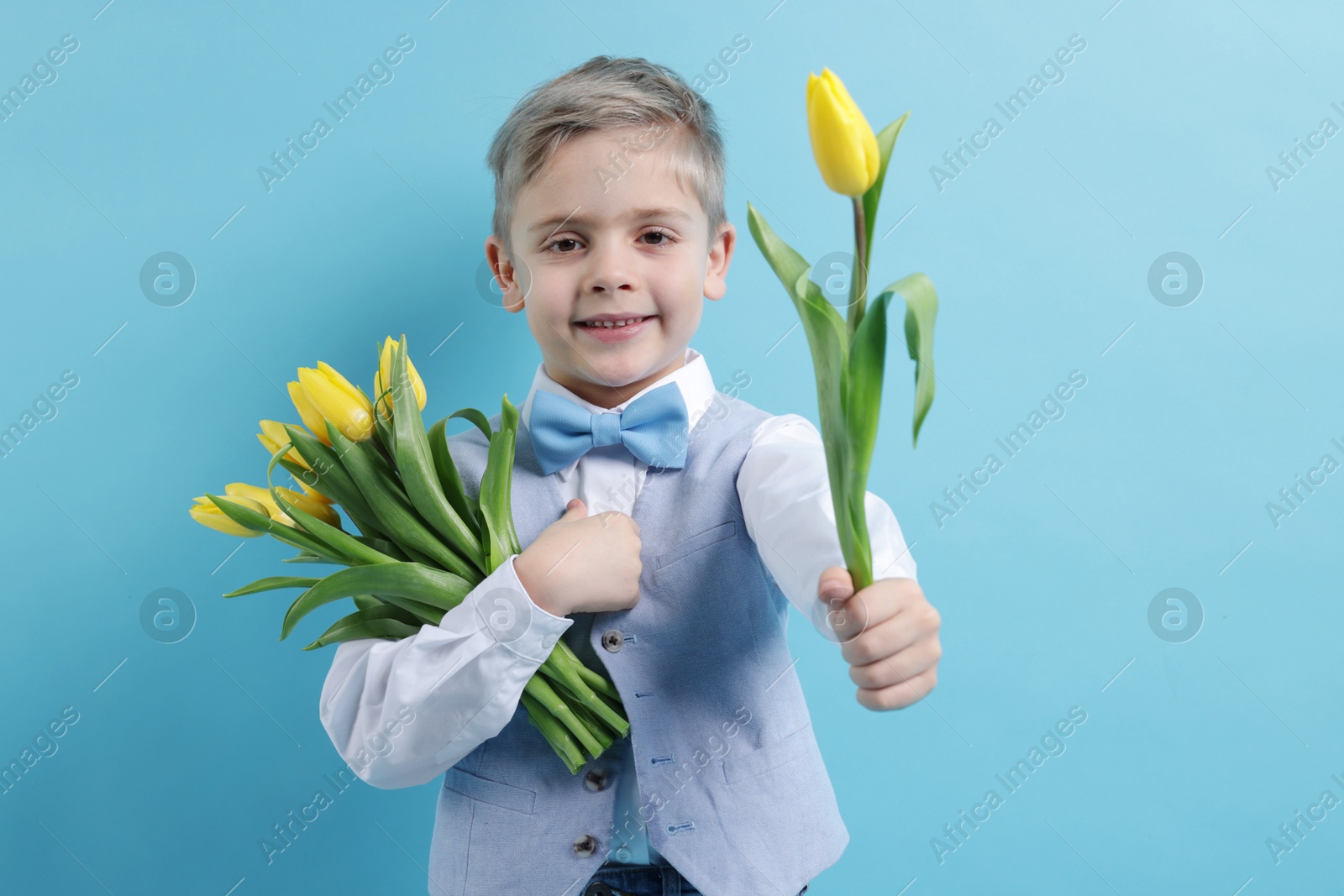 Photo of Cute little boy with bouquet of tulips on light blue background