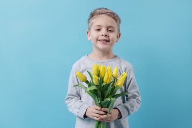 Cute little boy with bouquet of tulips on light blue background