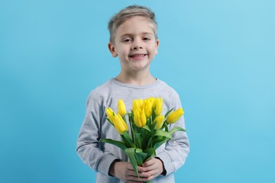 Cute little boy with bouquet of tulips on light blue background