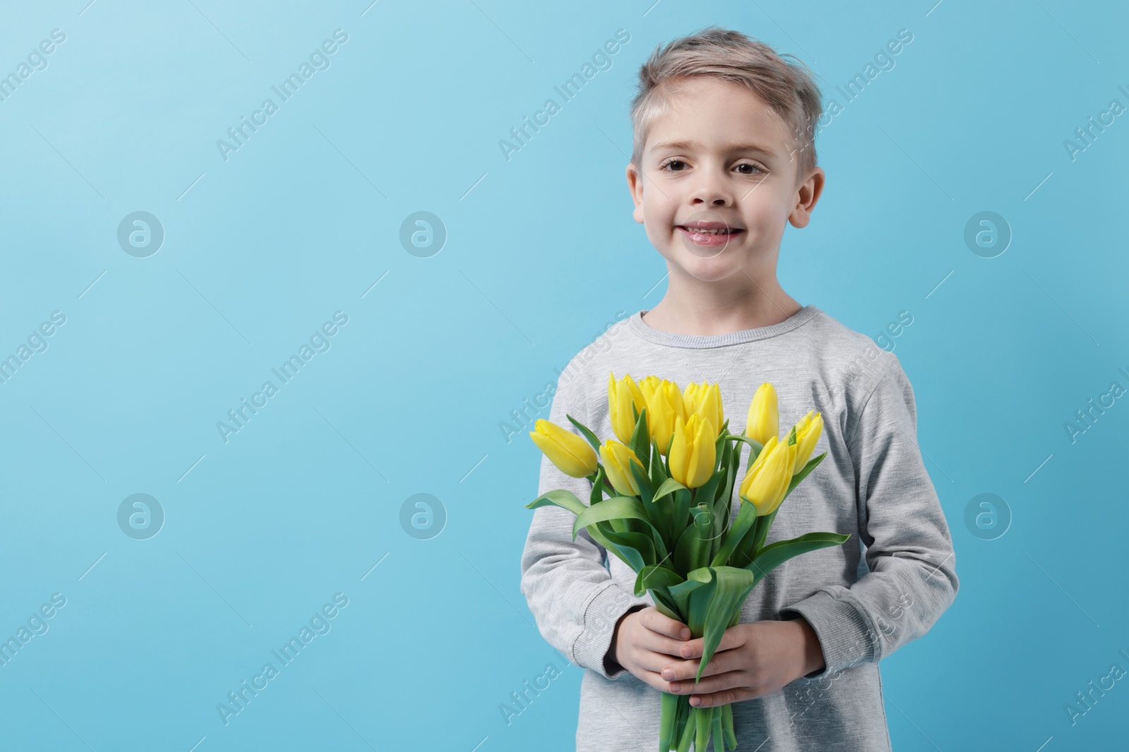 Photo of Cute little boy with bouquet of tulips on light blue background. Space for text