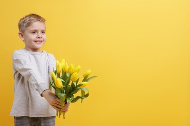 Cute little boy with bouquet of tulips on yellow background. Space for text