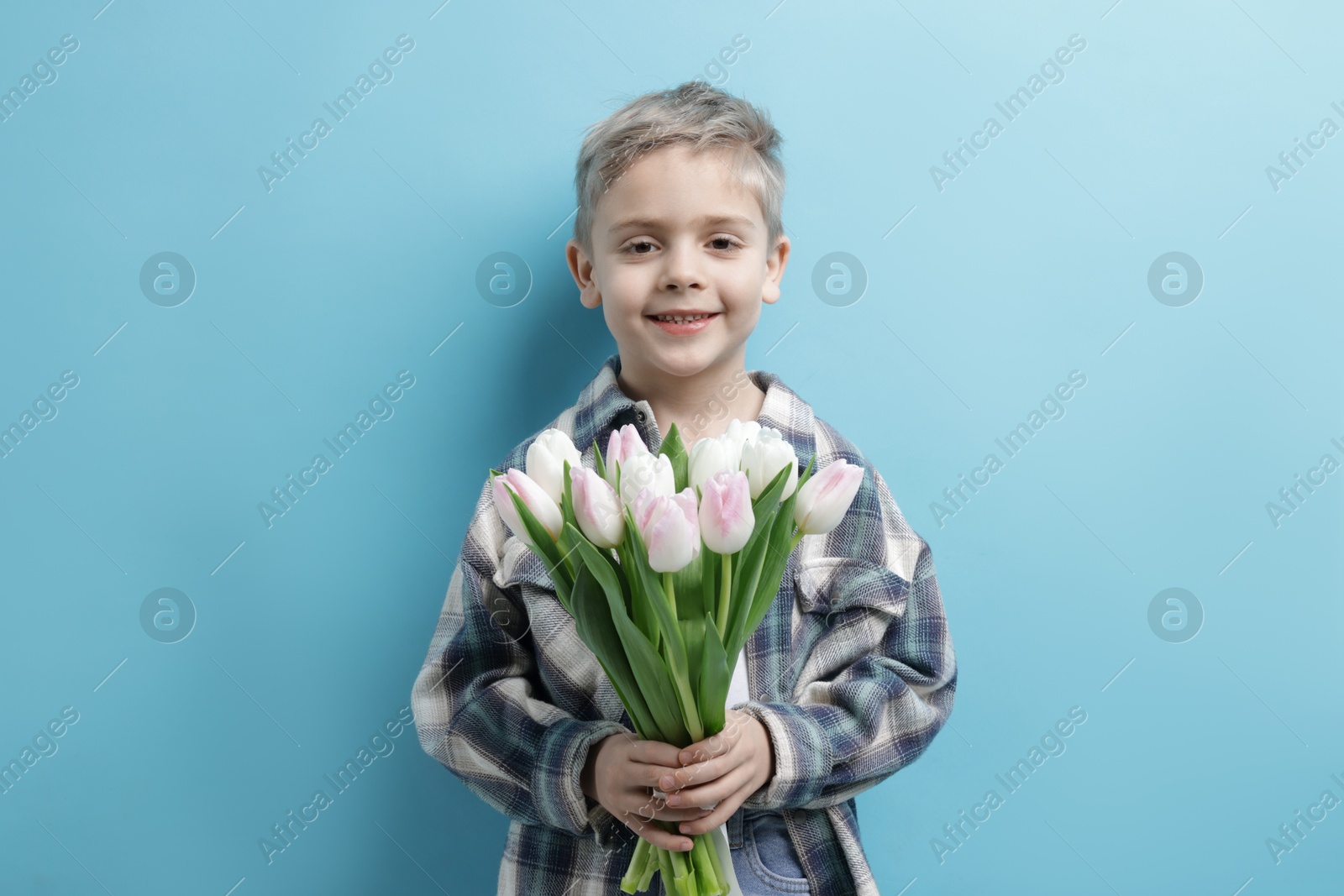 Photo of Cute little boy with bouquet of tulips on light blue background