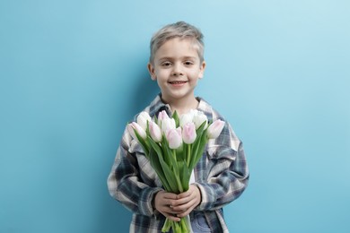 Cute little boy with bouquet of tulips on light blue background