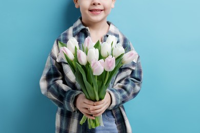 Photo of Little boy with bouquet of tulips on light blue background, closeup