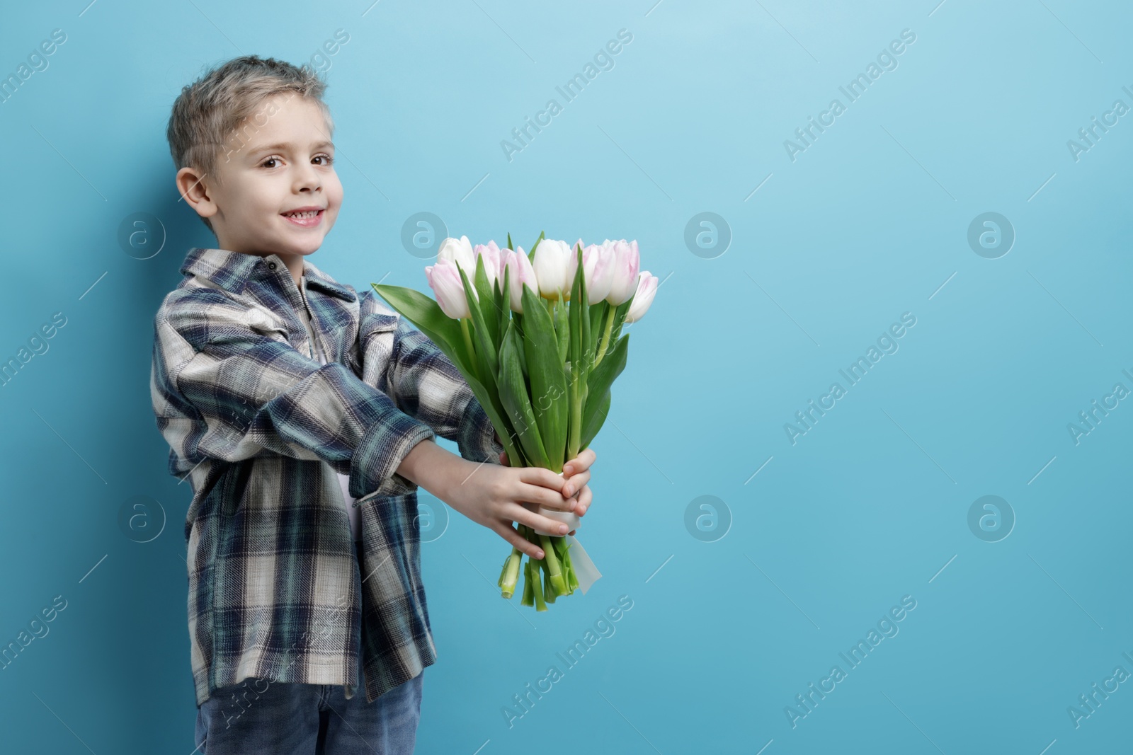 Photo of Cute little boy with bouquet of tulips on light blue background. Space for text