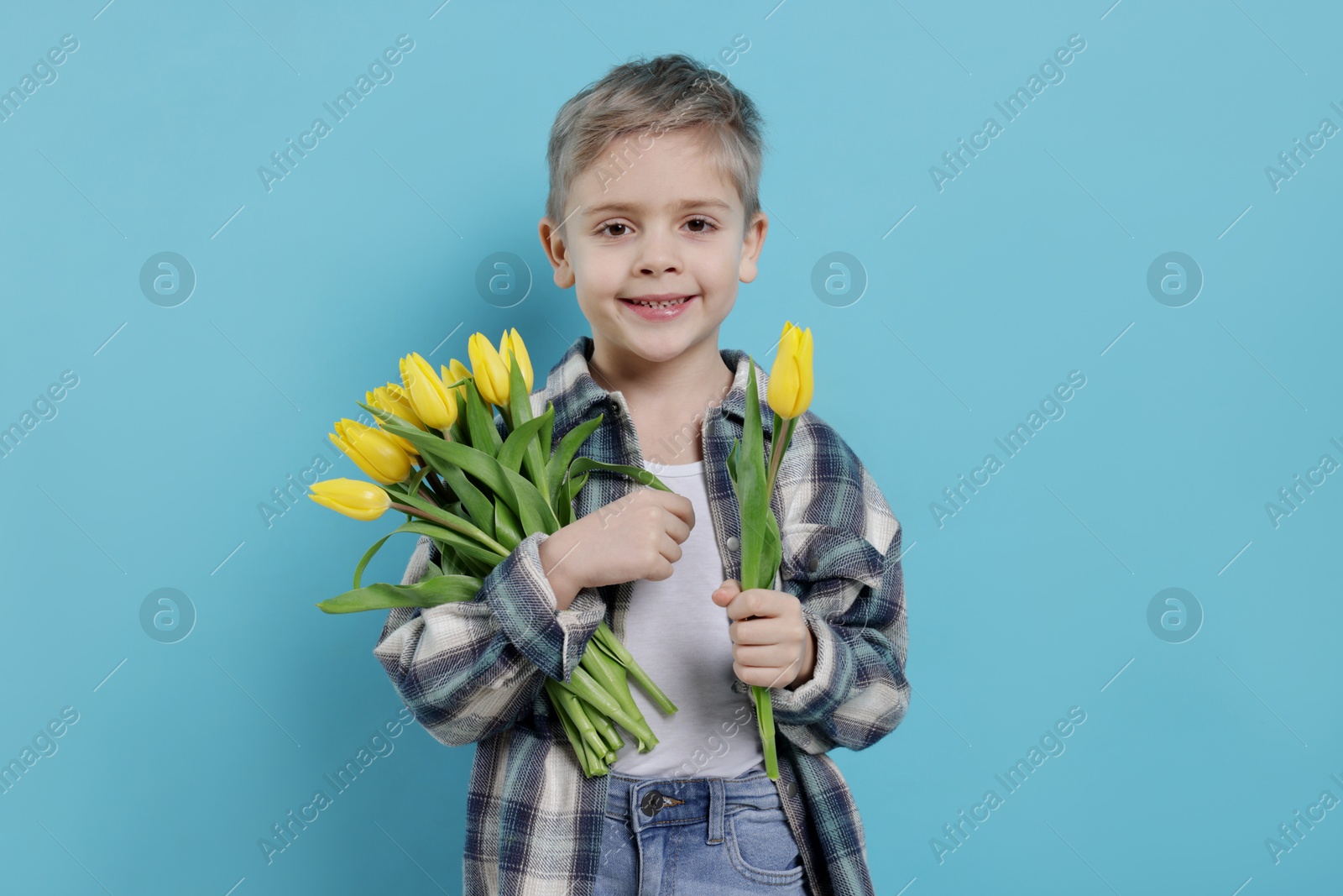 Photo of Cute little boy with bouquet of tulips on light blue background