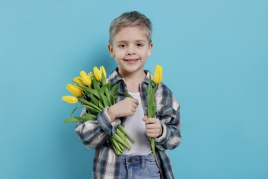 Cute little boy with bouquet of tulips on light blue background