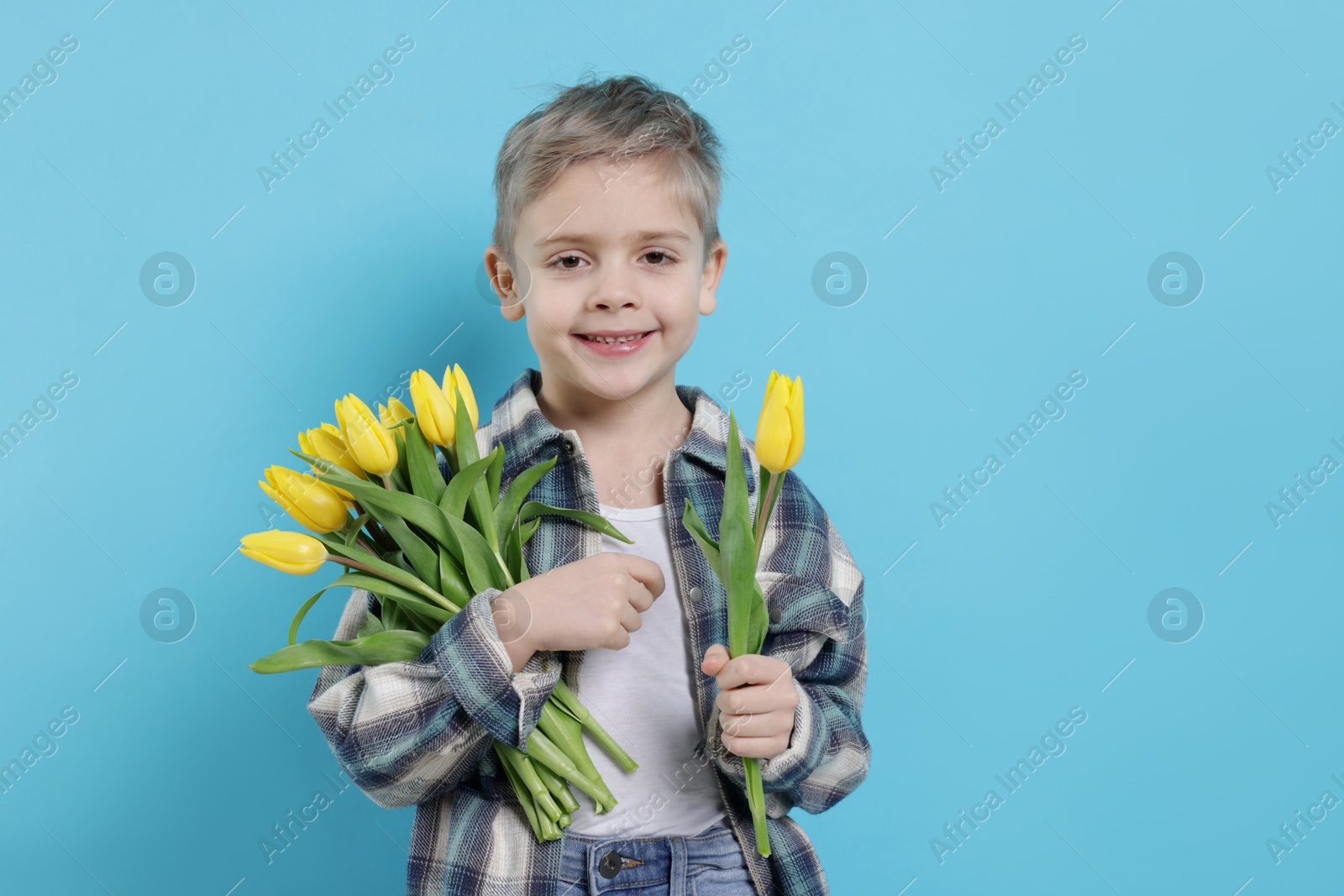 Photo of Cute little boy with bouquet of tulips on light blue background. Space for text