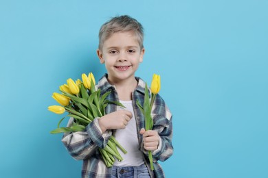 Cute little boy with bouquet of tulips on light blue background. Space for text