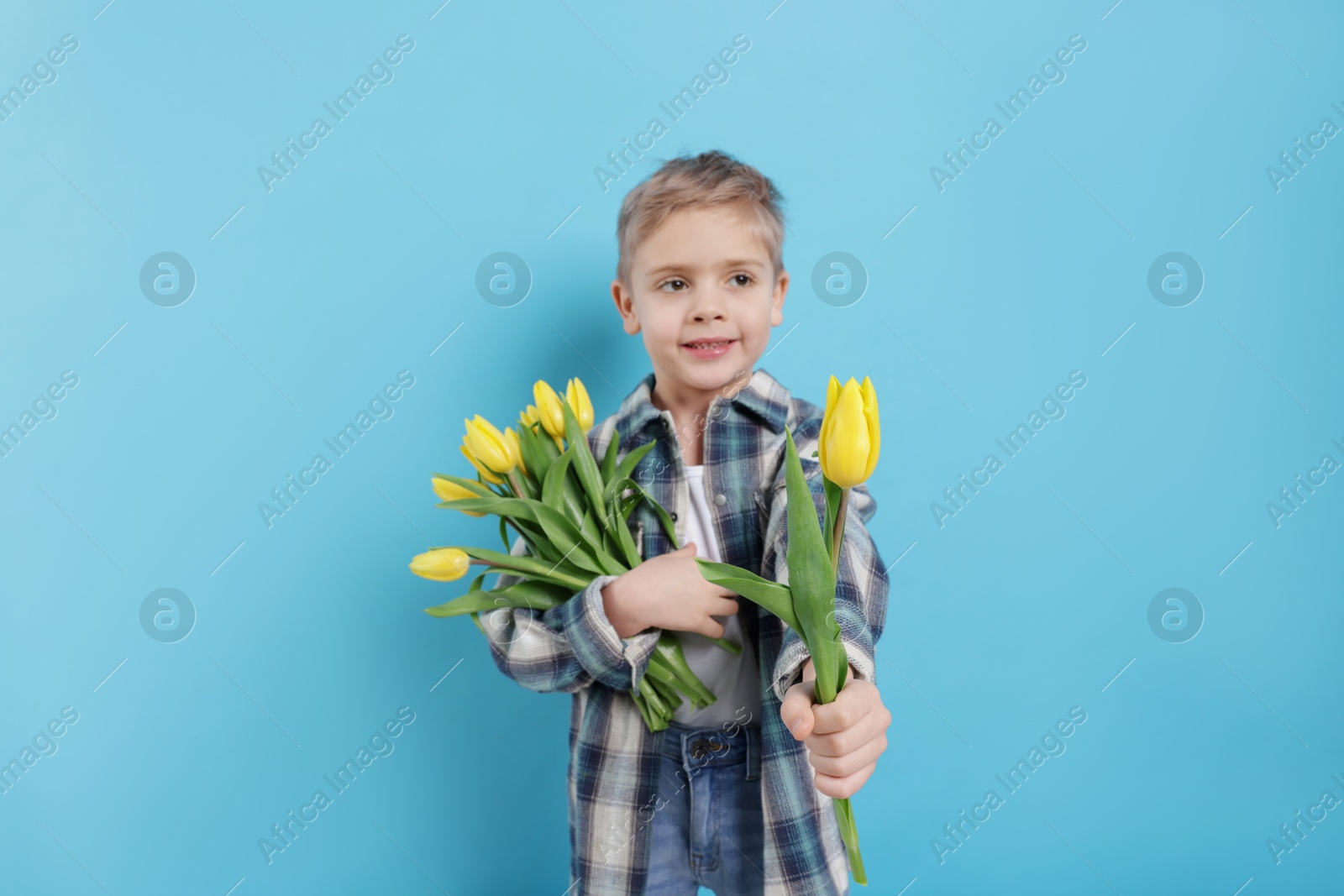 Photo of Cute little boy with bouquet of tulips on light blue background