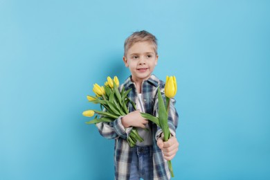 Photo of Cute little boy with bouquet of tulips on light blue background