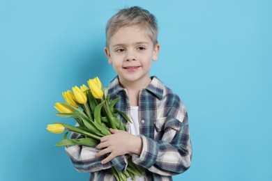 Photo of Cute little boy with bouquet of tulips on light blue background