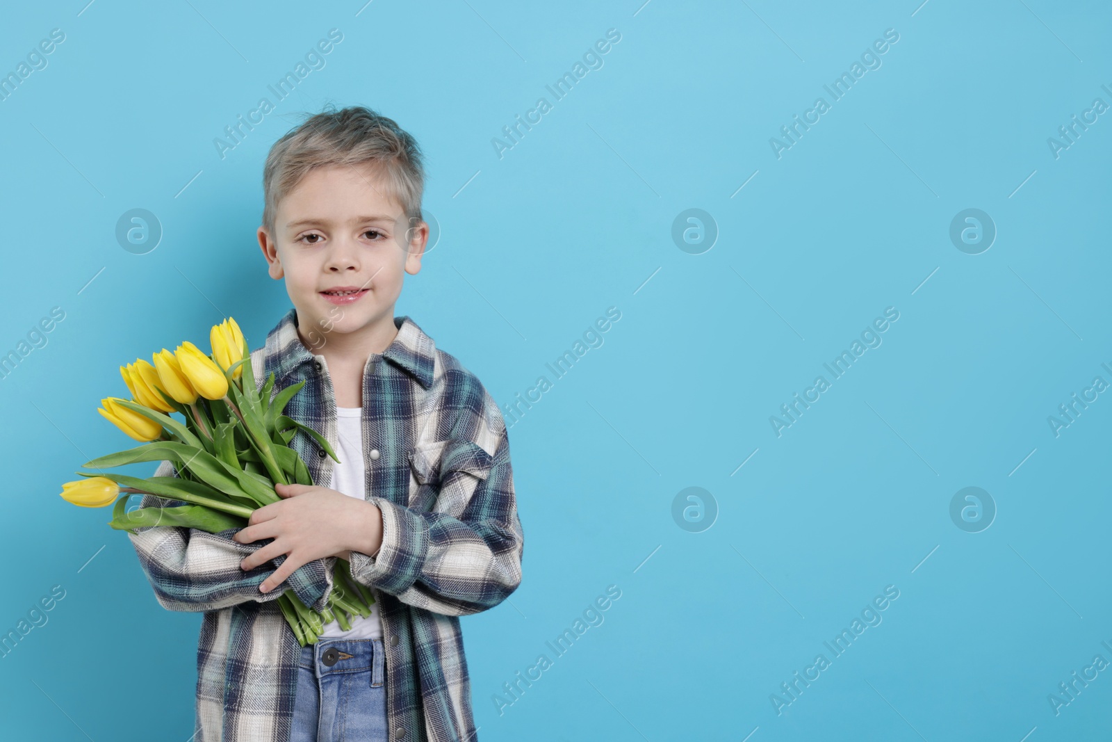 Photo of Cute little boy with bouquet of tulips on light blue background. Space for text