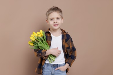 Photo of Cute little boy with bouquet of tulips on brown background