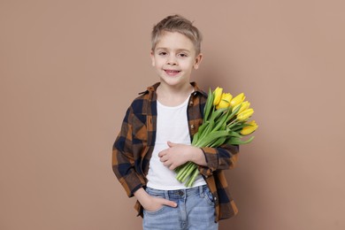 Photo of Cute little boy with bouquet of tulips on brown background