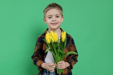 Cute little boy with bouquet of tulips on green background