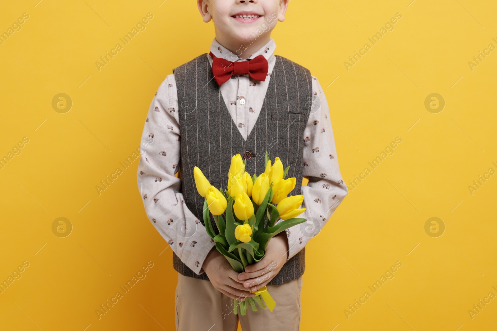 Photo of Little boy with bouquet of tulips on yellow background, closeup