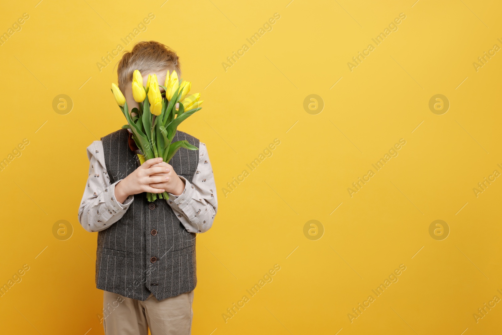 Photo of Little boy hiding behind bouquet of tulips on yellow background. Space for text