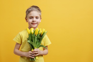 Photo of Cute little boy with bouquet of tulips on yellow background. Space for text