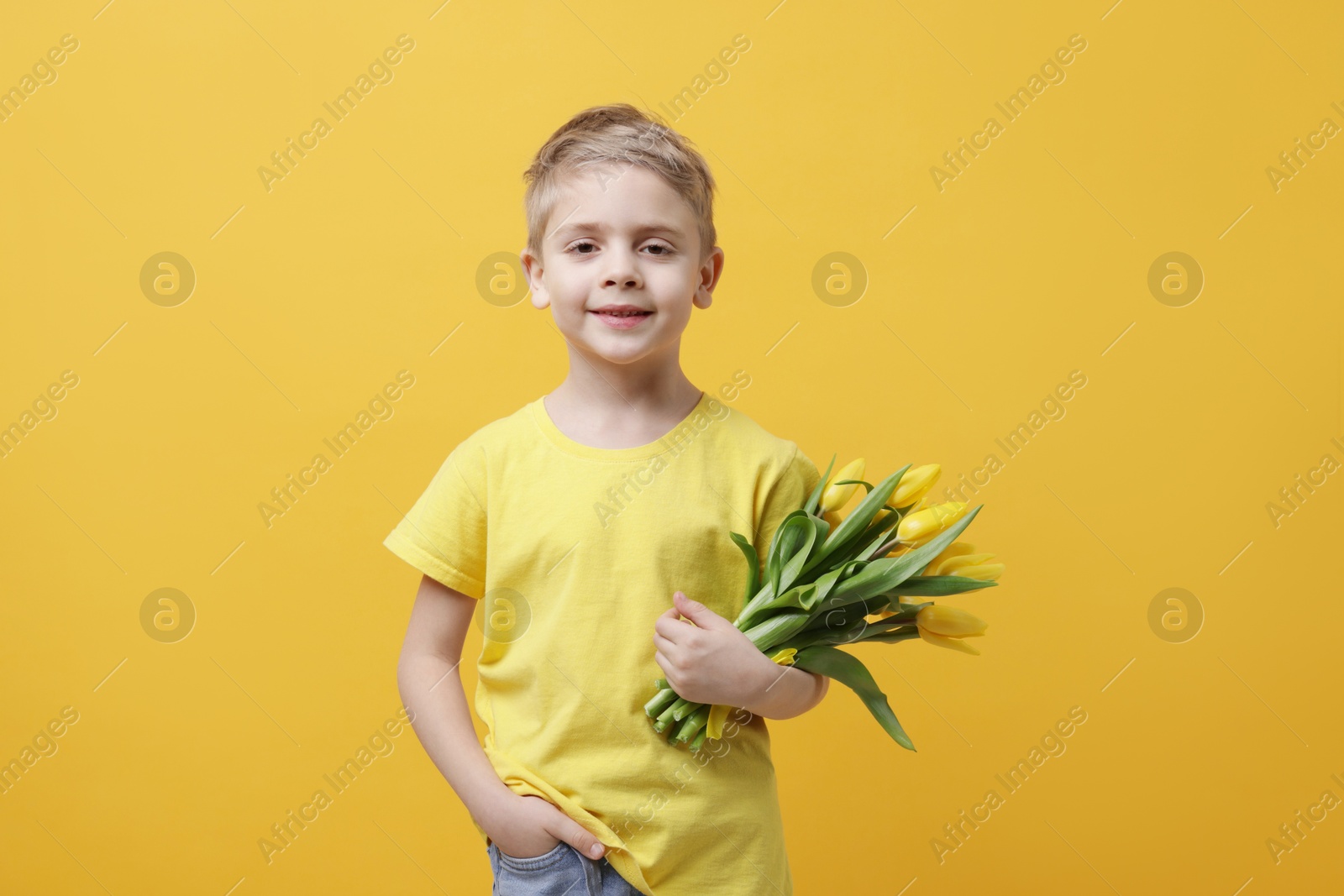 Photo of Cute little boy with bouquet of tulips on yellow background