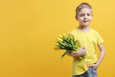 Photo of Cute little boy with bouquet of tulips on yellow background. Space for text