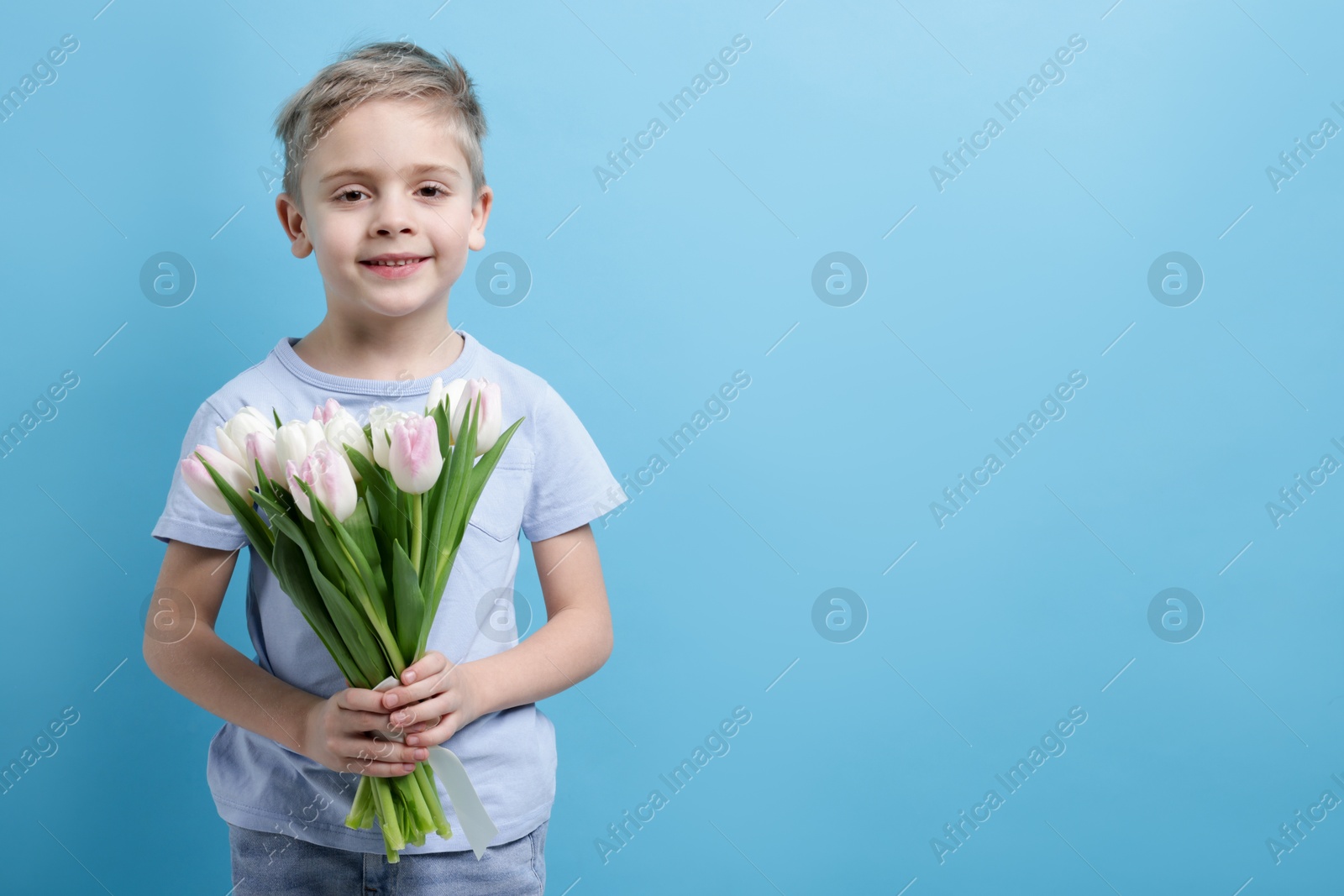 Photo of Cute little boy with bouquet of tulips on light blue background. Space for text