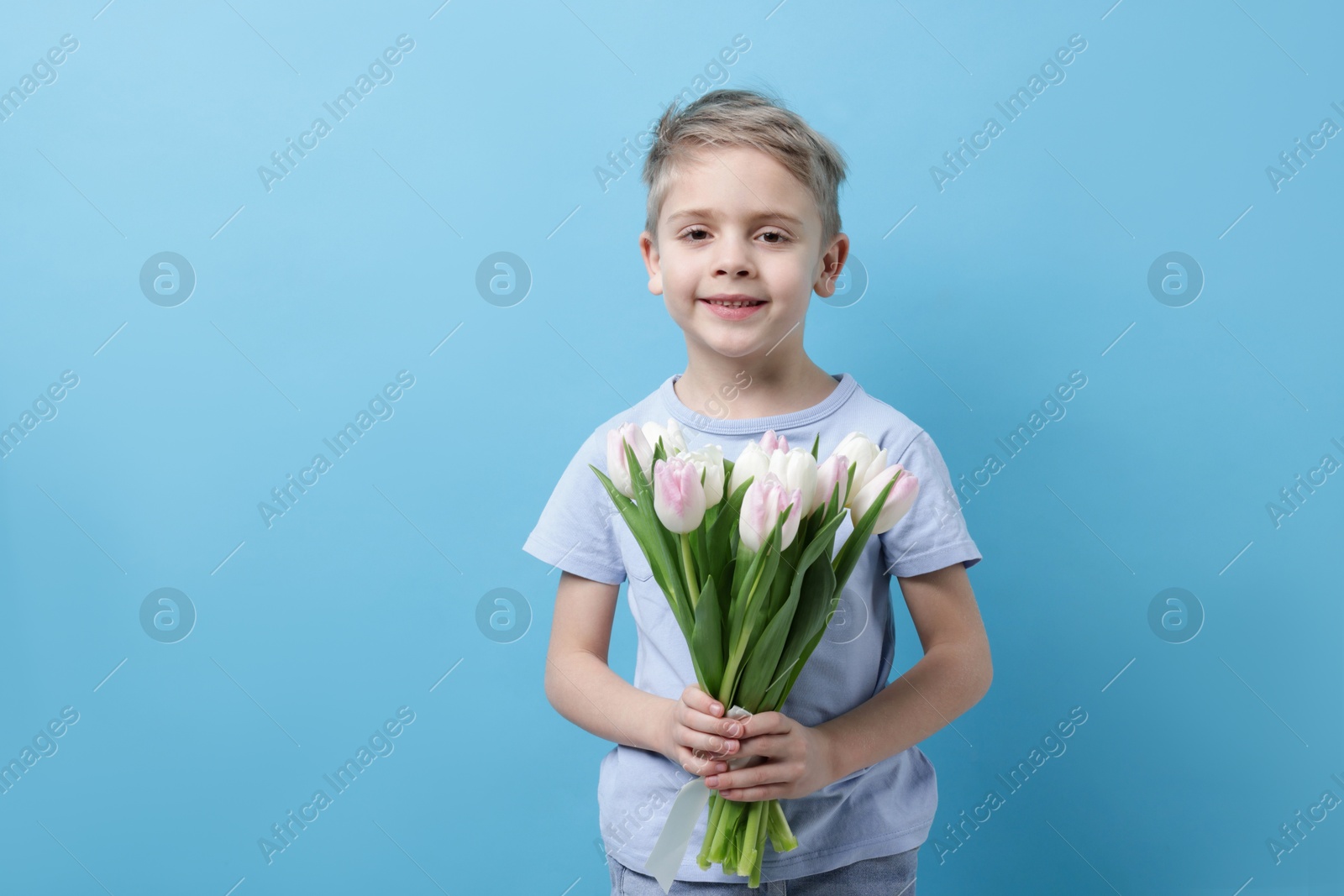 Photo of Cute little boy with bouquet of tulips on light blue background. Space for text