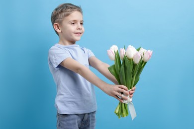 Cute little boy with bouquet of tulips on light blue background