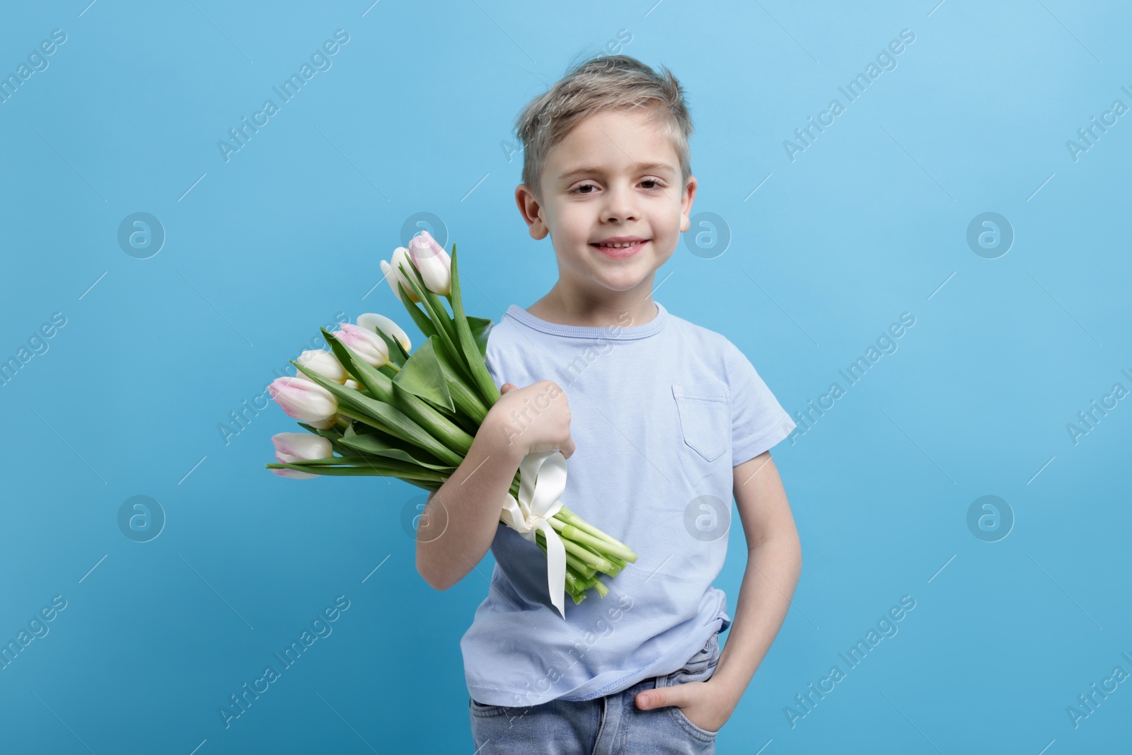 Photo of Cute little boy with bouquet of tulips on light blue background