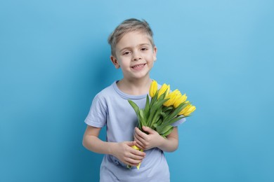 Photo of Cute little boy with bouquet of tulips on light blue background