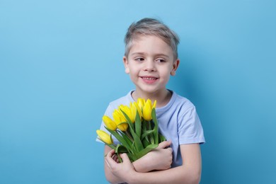 Photo of Cute little boy with bouquet of tulips on light blue background. Space for text