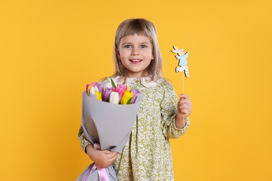 Photo of Smiling little girl with bouquet of tulips and decorative Easter bunny on orange background