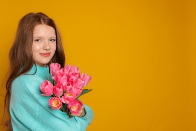 Photo of Beautiful teenage girl with bouquet of tulips on orange background, space for text