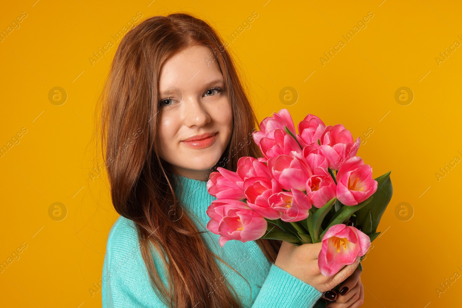 Photo of Beautiful teenage girl with bouquet of tulips on orange background