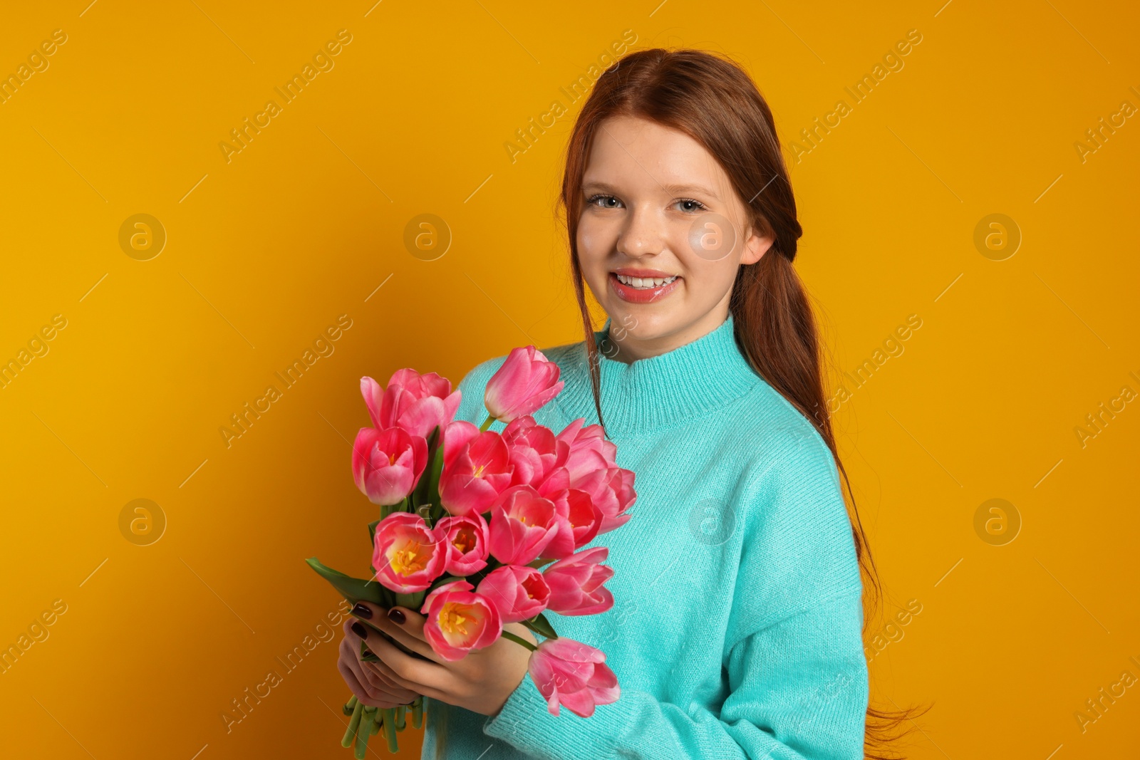 Photo of Beautiful teenage girl with bouquet of tulips on orange background