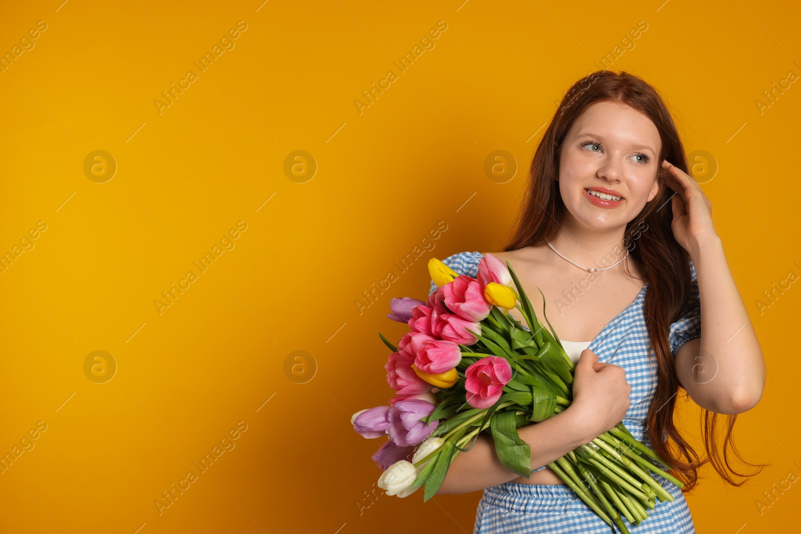 Photo of Beautiful teenage girl with bouquet of tulips on orange background, space for text