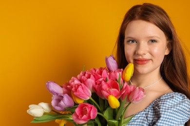 Photo of Beautiful teenage girl with bouquet of tulips on orange background, space for text