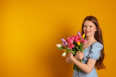 Photo of Beautiful teenage girl with bouquet of tulips on orange background, space for text