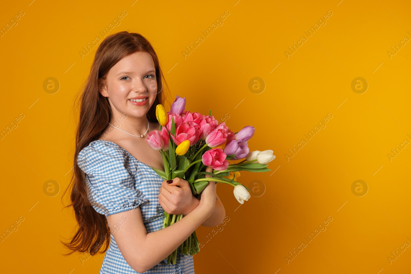 Photo of Beautiful teenage girl with bouquet of tulips on orange background, space for text