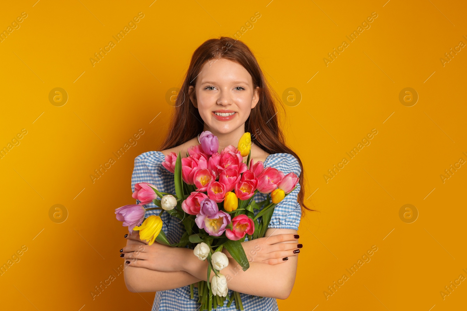 Photo of Beautiful teenage girl with bouquet of tulips on orange background