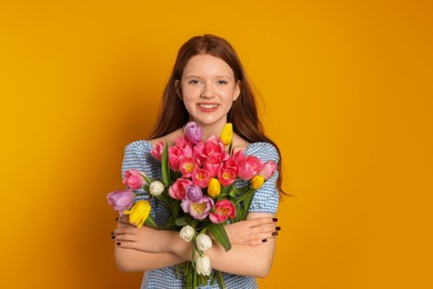 Photo of Beautiful teenage girl with bouquet of tulips on orange background