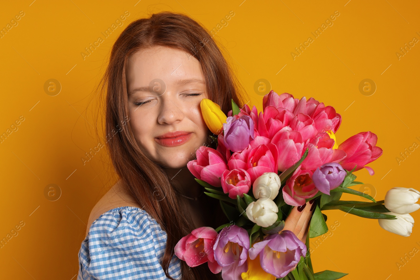 Photo of Beautiful teenage girl with bouquet of tulips on orange background