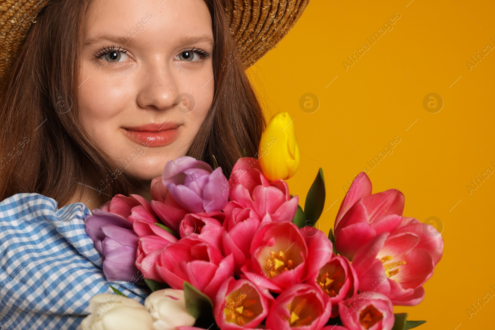 Photo of Beautiful teenage girl with bouquet of tulips on orange background, closeup