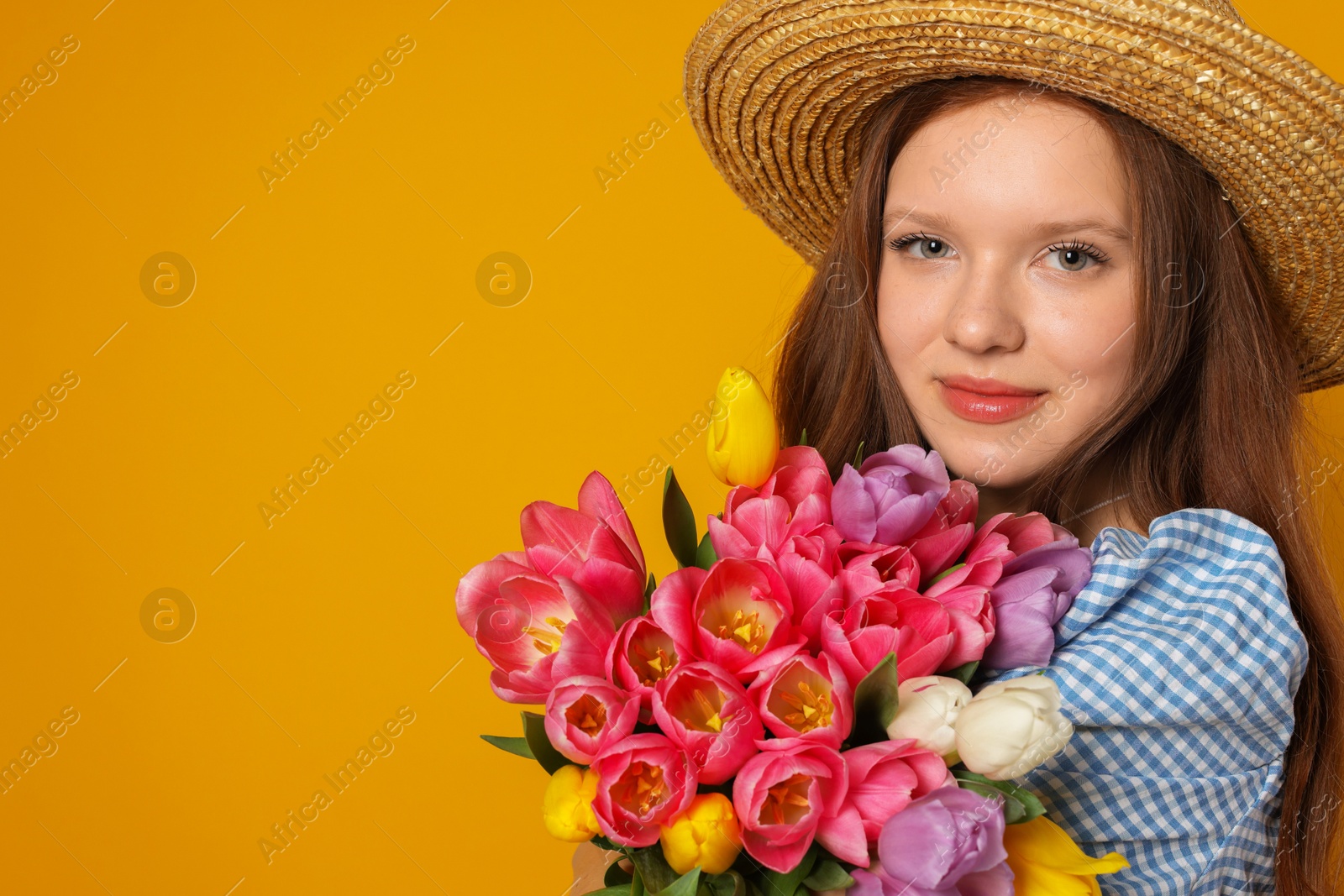 Photo of Beautiful teenage girl with bouquet of tulips on orange background, space for text