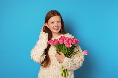 Photo of Beautiful teenage girl with bouquet of tulips on light blue background