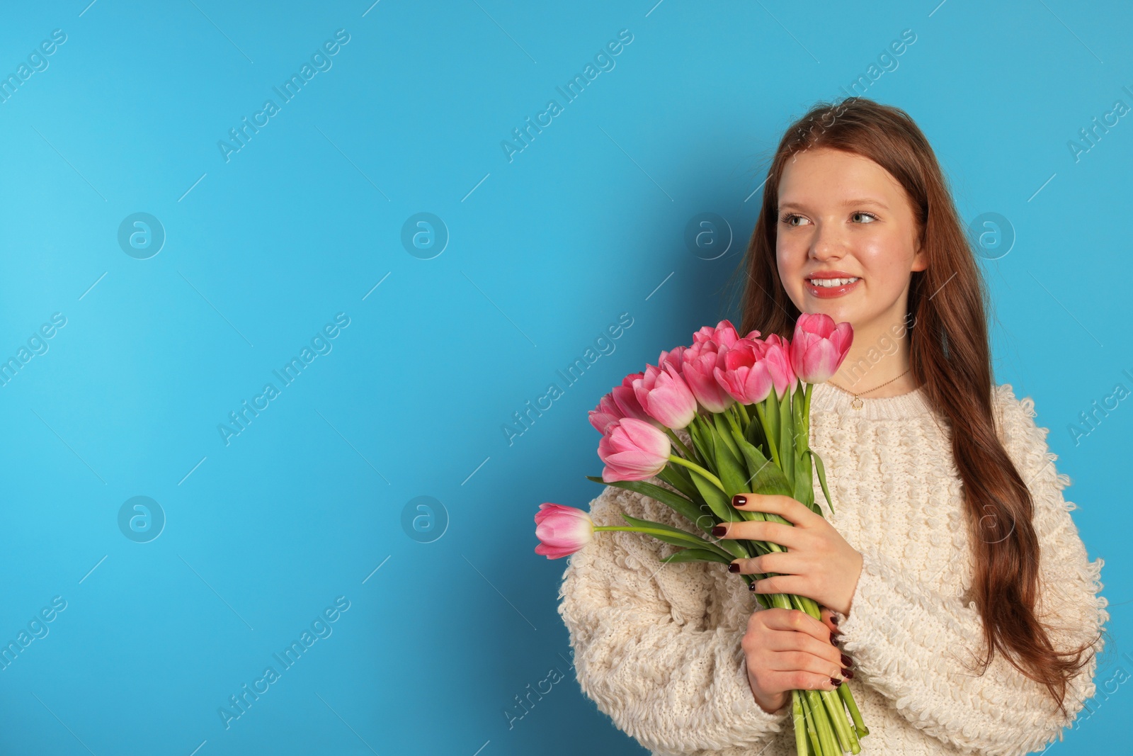 Photo of Beautiful teenage girl with bouquet of tulips on light blue background, space for text