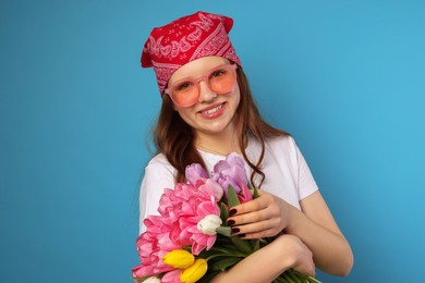 Photo of Beautiful teenage girl with bouquet of tulips on light blue background